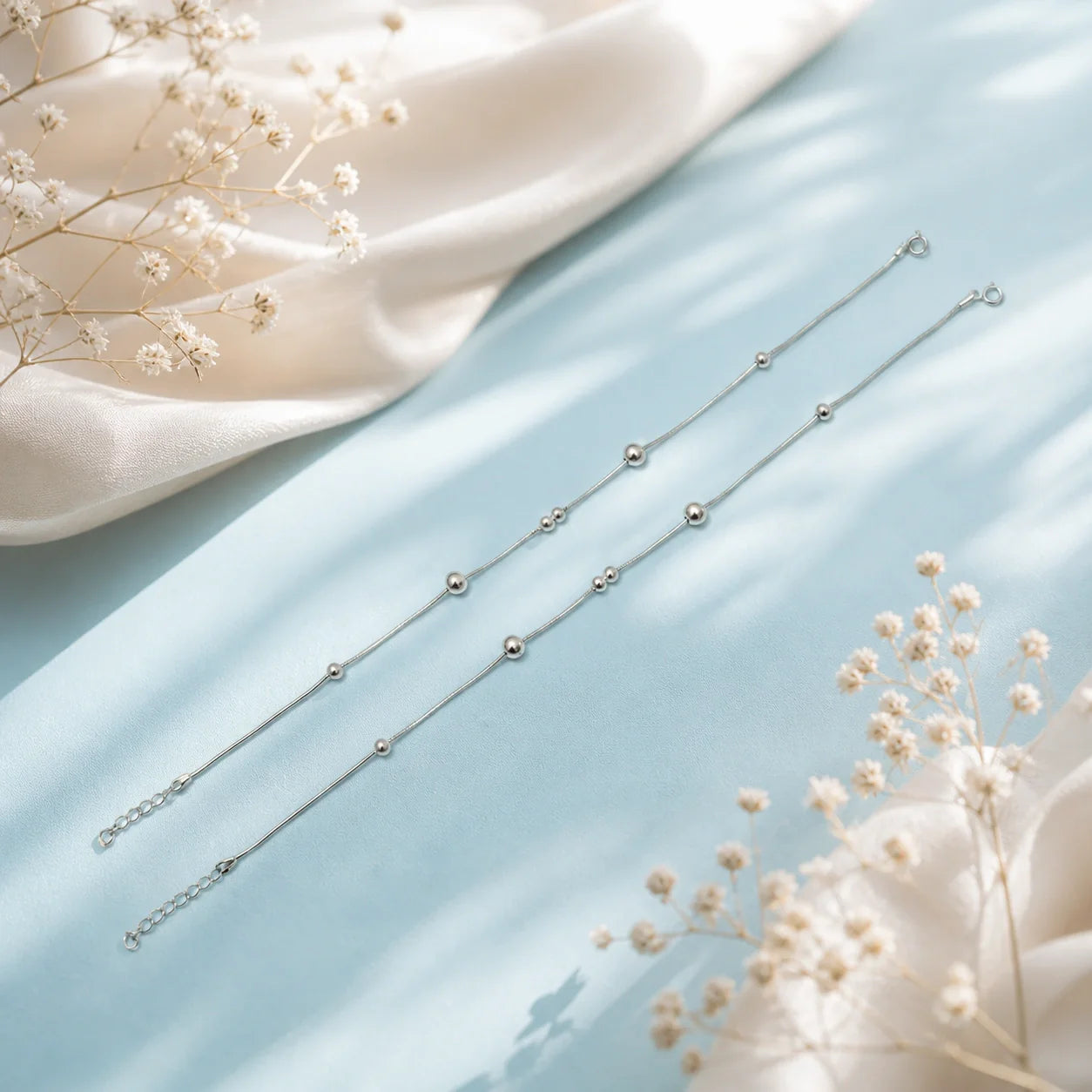 Pair of beaded anklets on light bluish background 