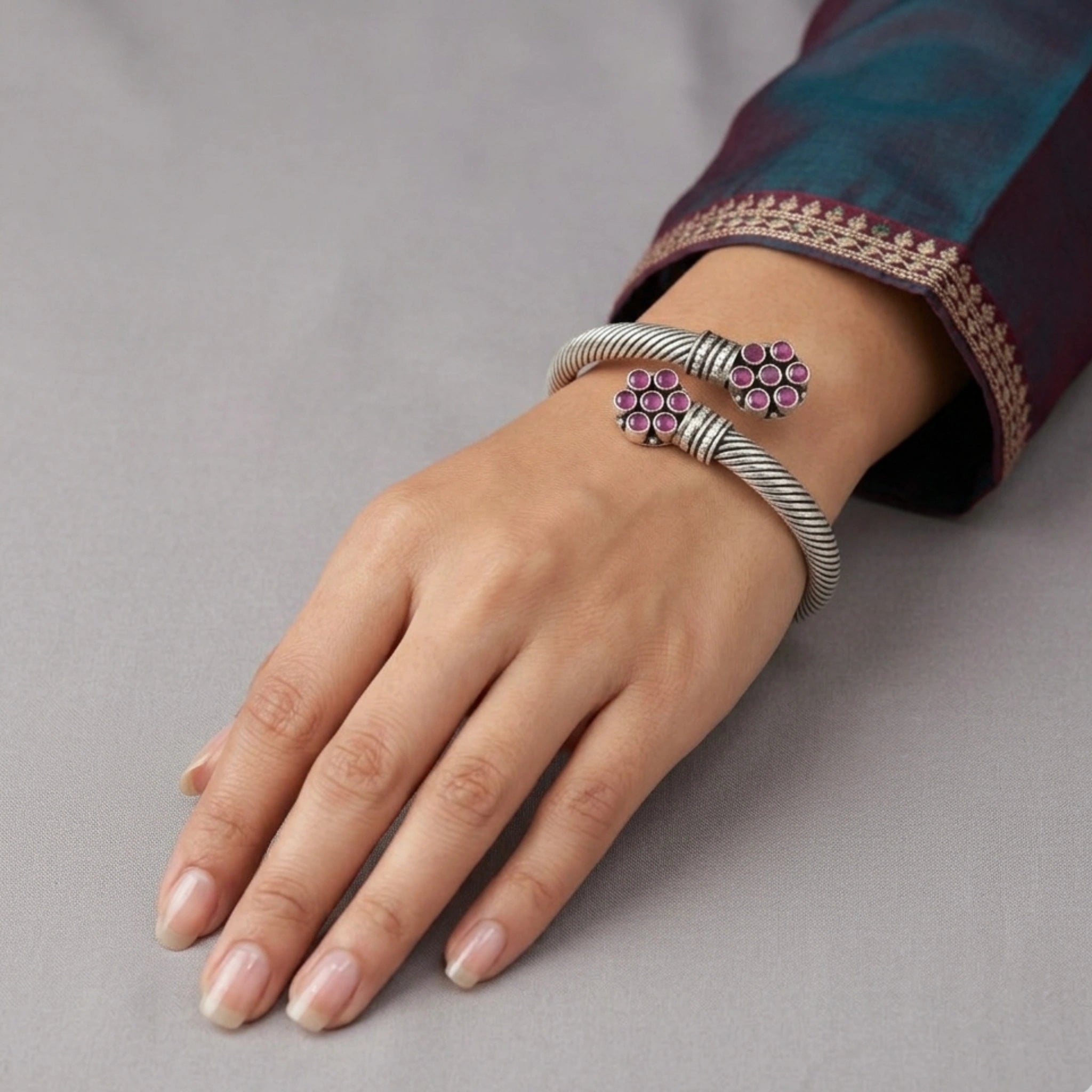 Hand wearing a silver bracelet with pink gemstones on a gray background