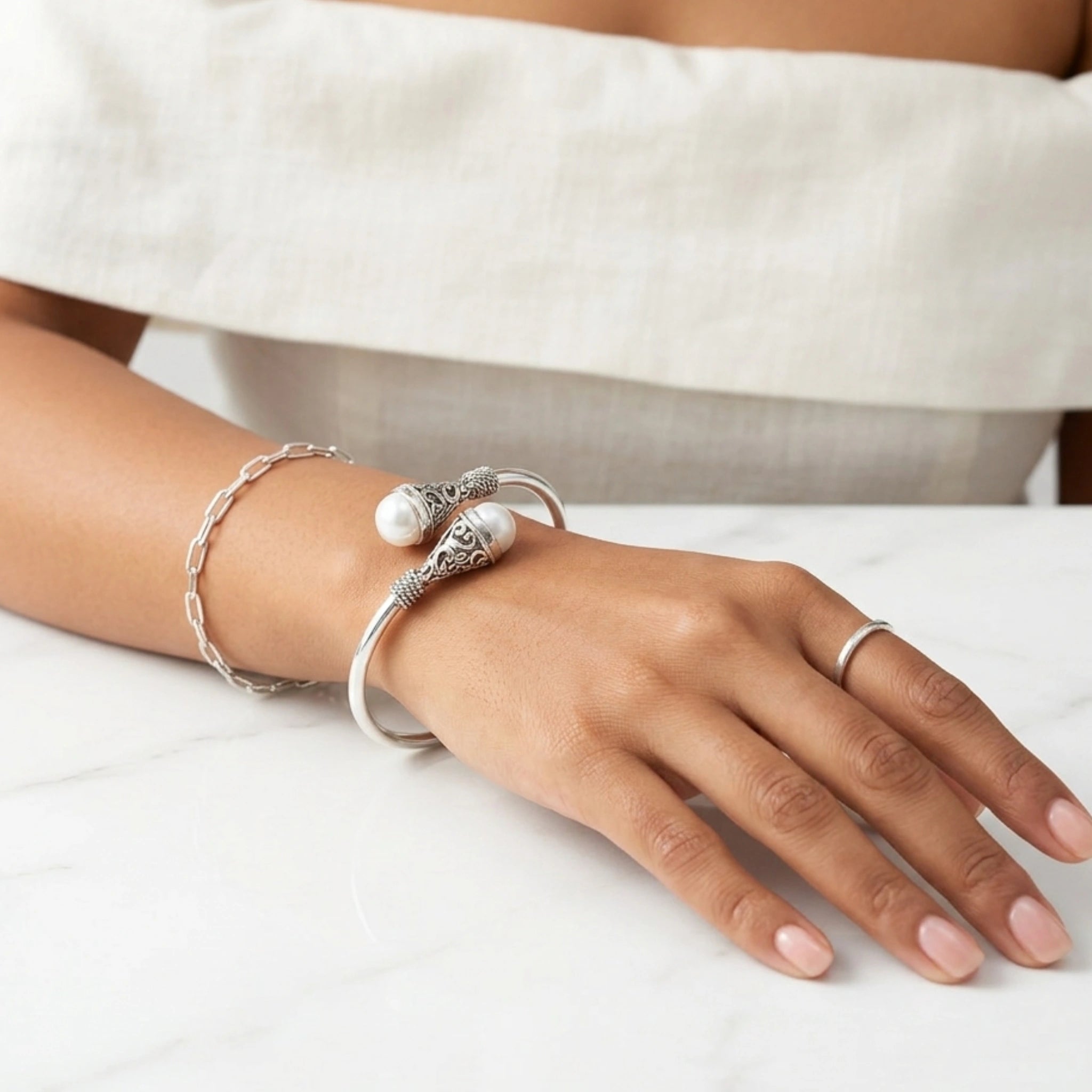 Hand wearing silver bracelet and ring on a white surface