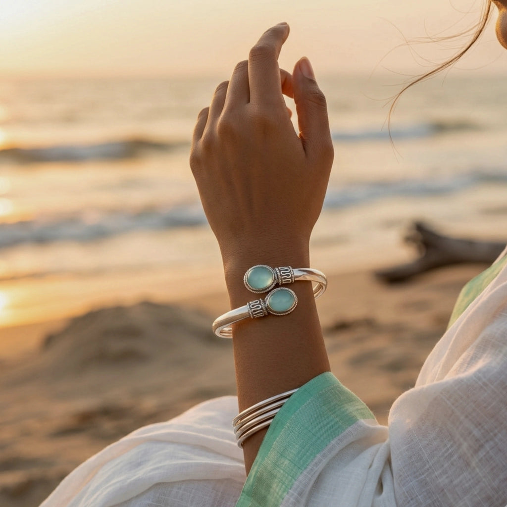 Person wearing silver bracelets with turquoise stones on a beach at sunset