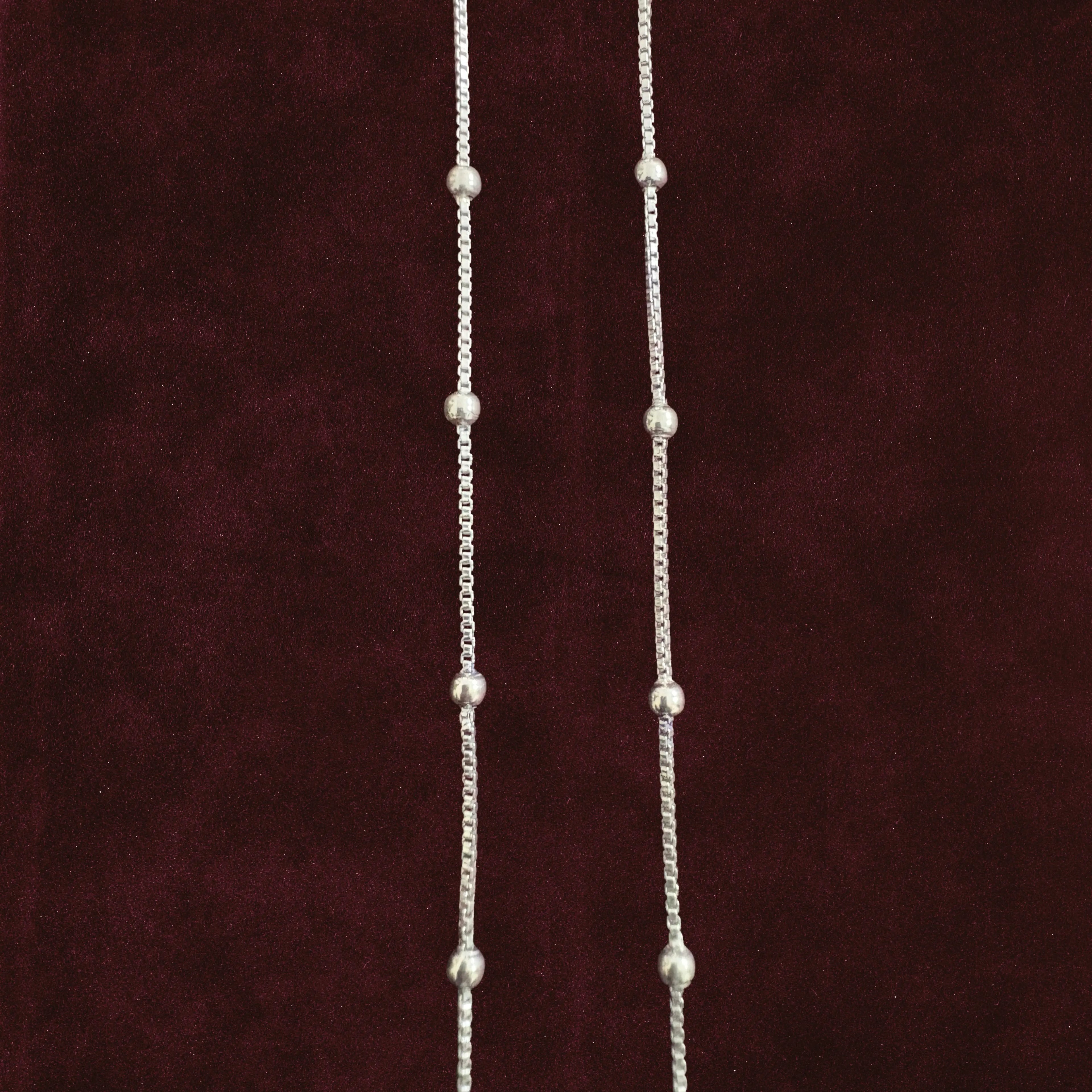 Silver dew drop anklet pair closeup on solid background