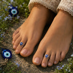 Feet with blue evil eye rings on toes, surrounded by flowers and stones.