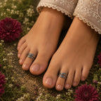 Close-up of feet with silver rings on toes, surrounded by flowers and greenery