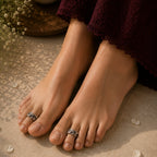 Close-up of feet with rings on toes, wearing a dark garment, on a textured surface.