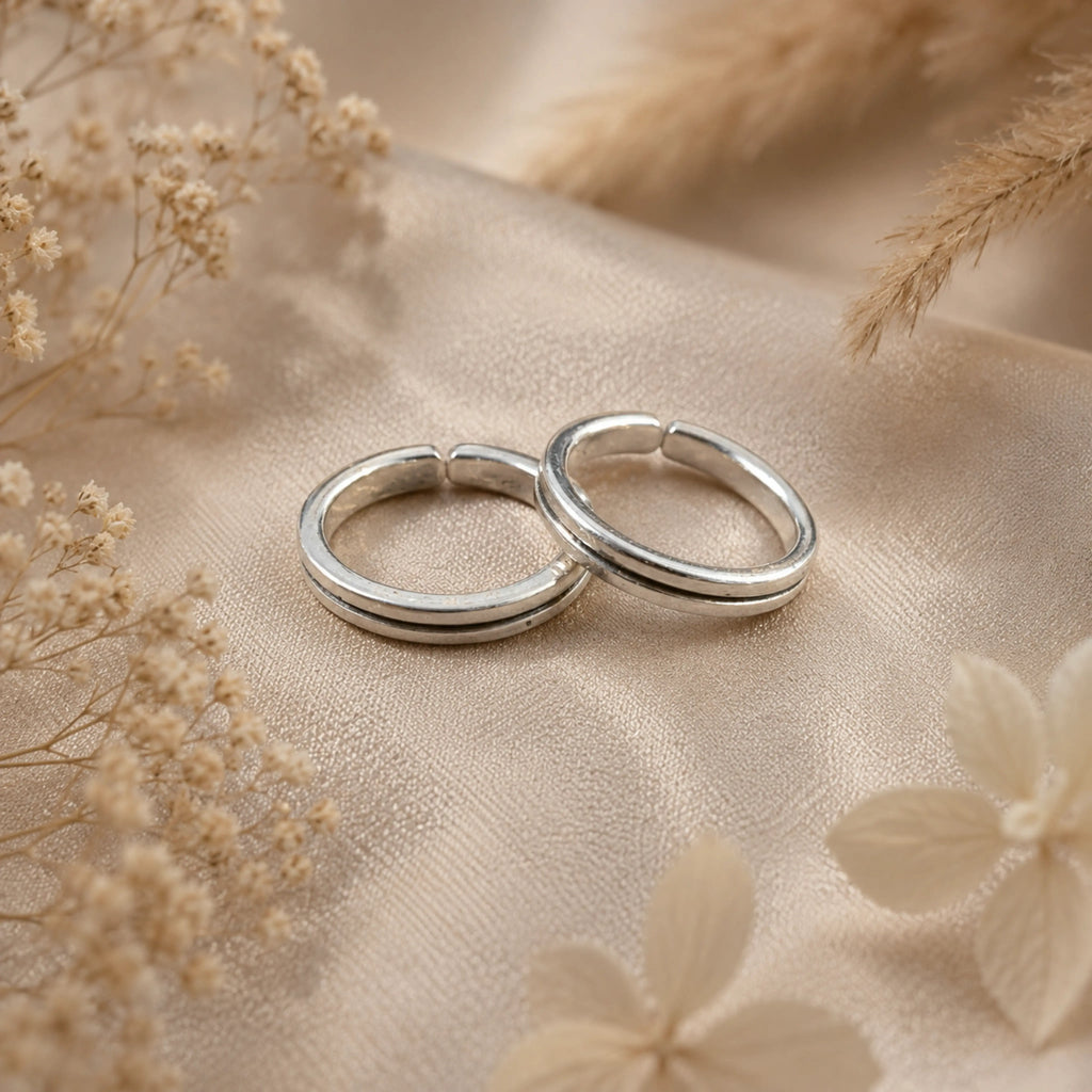 Two silver toe earrings on a beige fabric background with dried flowers.