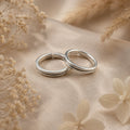 Two silver toe earrings on a beige fabric background with dried flowers.