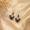 Ornate silver earrings with red stones on a beige fabric background