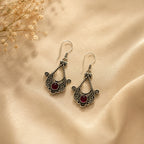Ornate silver earrings with red stones on a beige fabric background