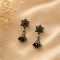 Pair of ornate earrings with green gemstones on a beige surface.