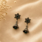 Pair of ornate earrings with green gemstones on a beige surface.