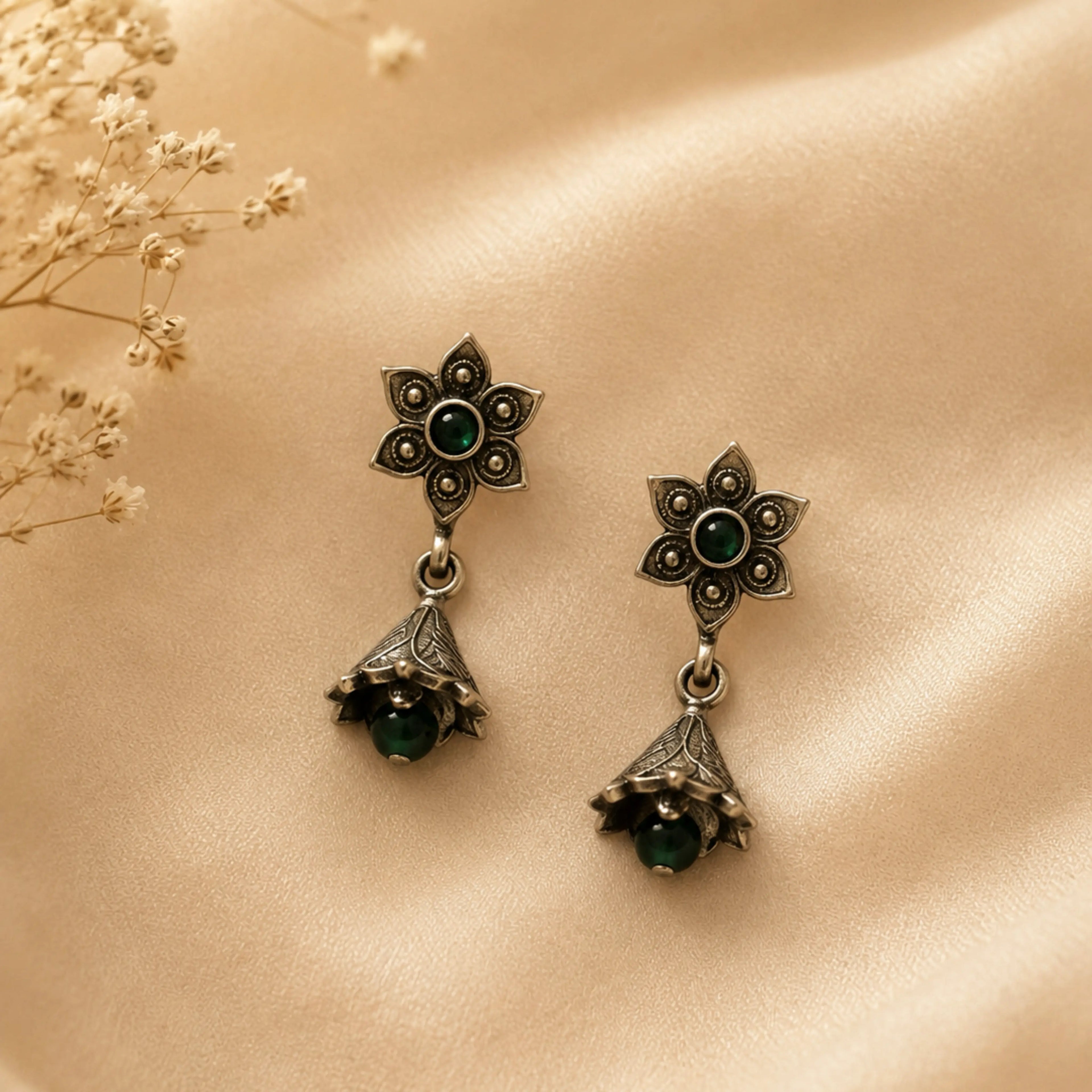 Pair of ornate earrings with green gemstones on a beige surface.