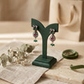 Pair of earrings on a green stand with a neutral background