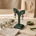 Pair of earrings on a green stand with a neutral background