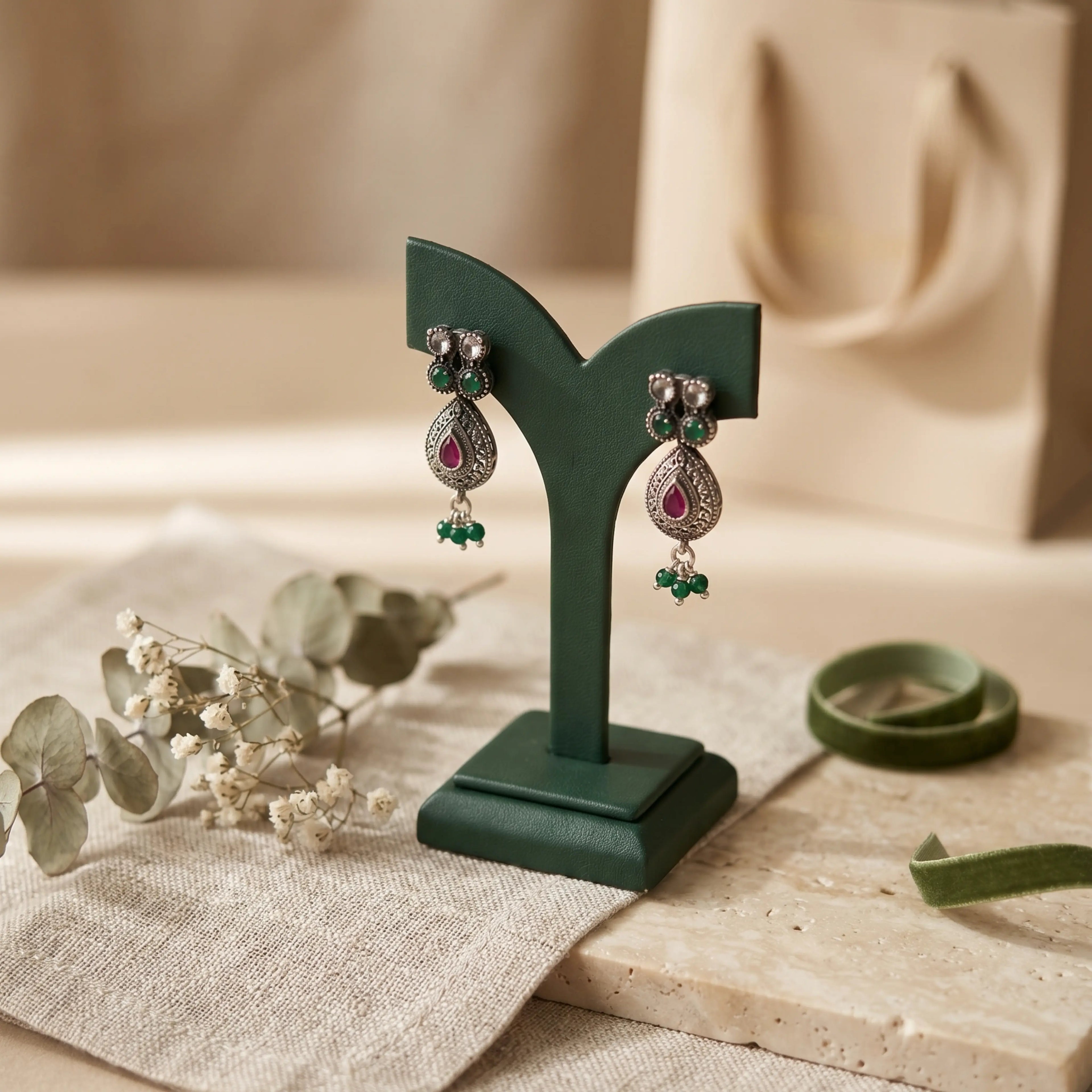 Pair of earrings on a green stand with a neutral background