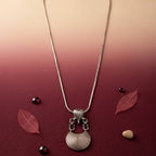 Silver necklace with a pendant on a maroon background with leaves and stones.