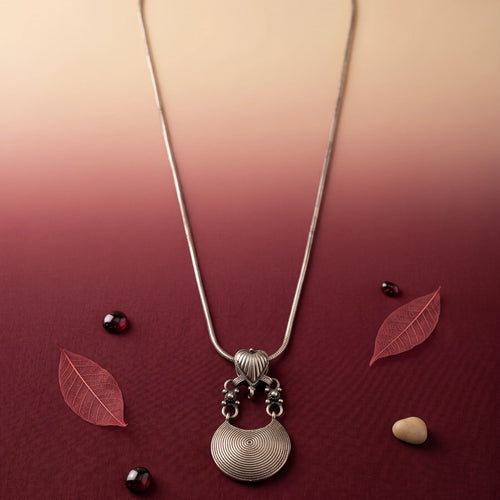 Silver necklace with a pendant on a maroon background with leaves and stones.