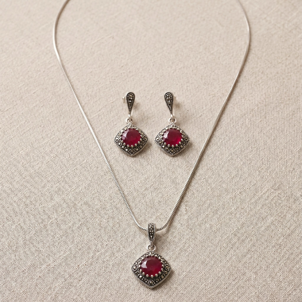 Jewelry set with necklace and earrings featuring red gemstones on a beige fabric background