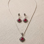 Jewelry set with necklace and earrings featuring red gemstones on a beige fabric background