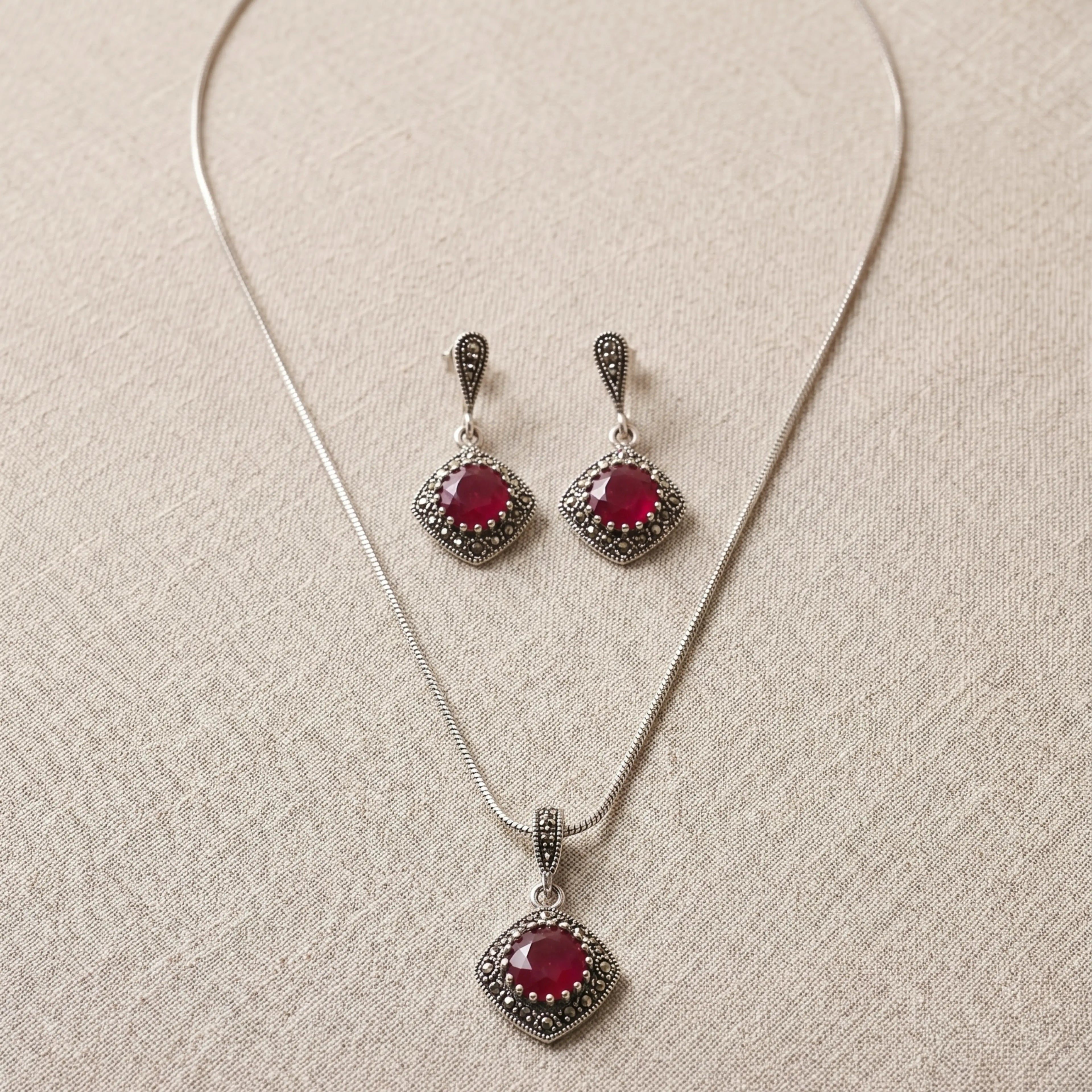 Jewelry set with necklace and earrings featuring red gemstones on a beige fabric background
