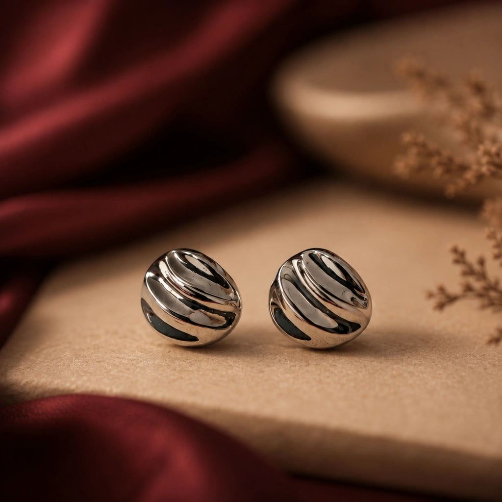 Silver striped earrings on a textured surface with red fabric and dried flowers in the background