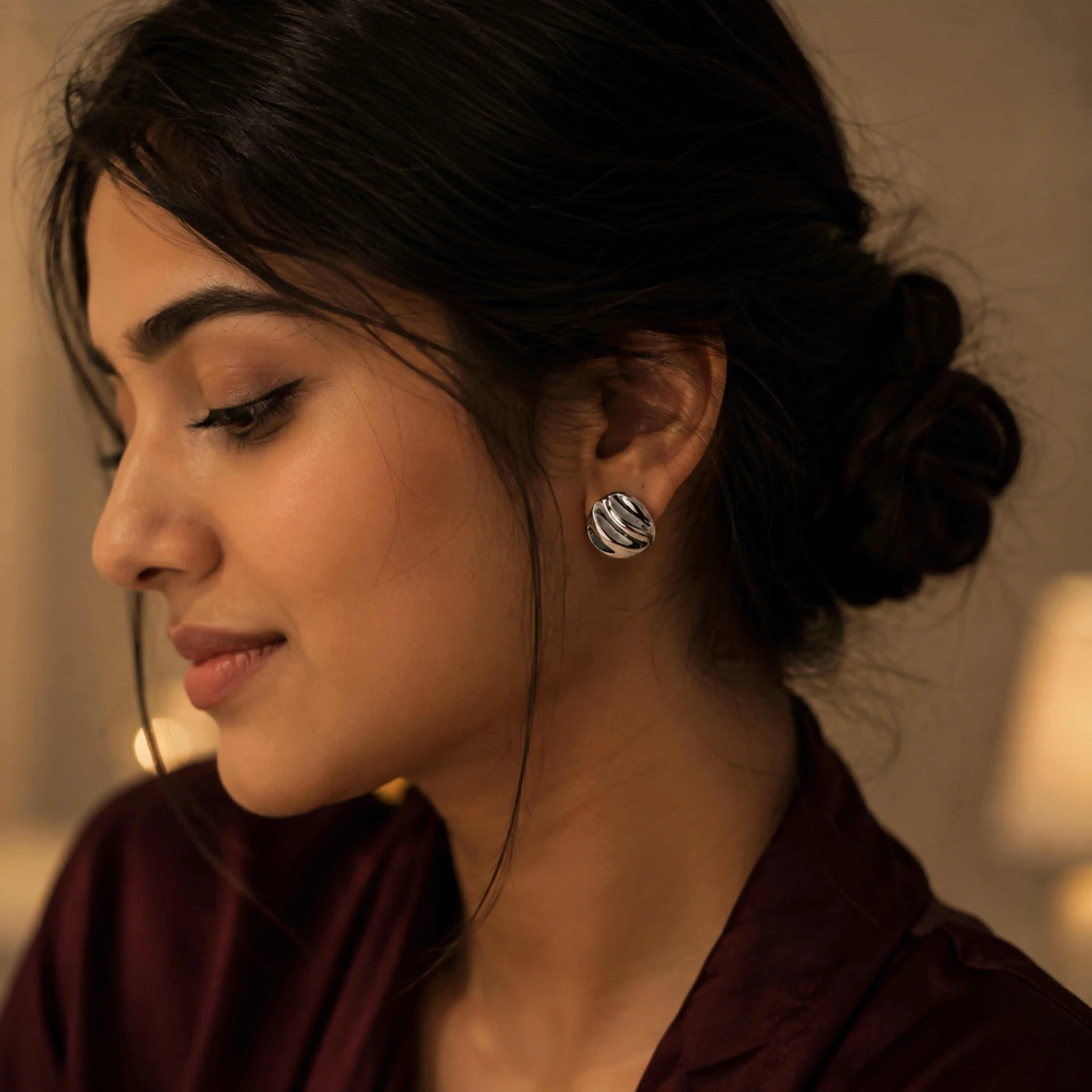 Woman wearing a dark brown garment with a blurred background showcasing silver ribbed earrings