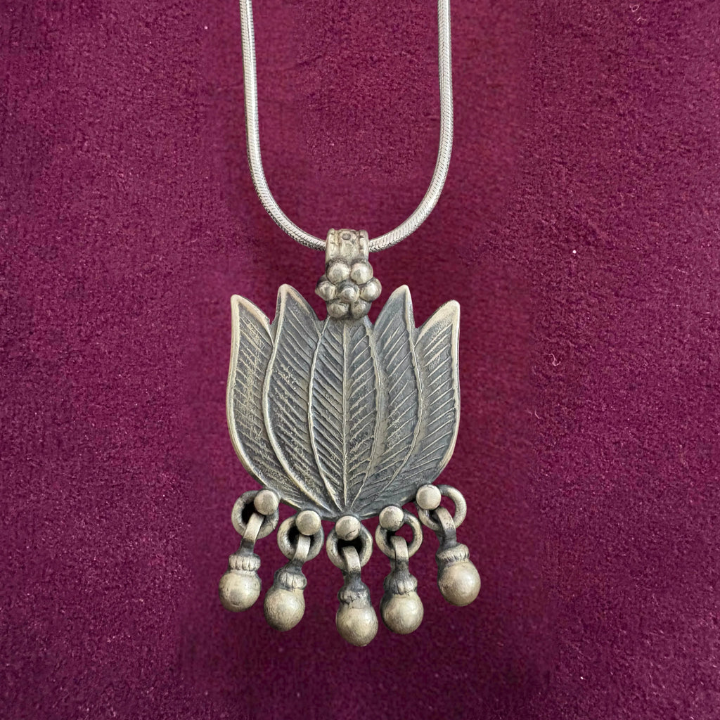 Silver necklace with a lotus-shaped pendant on a maroon background
