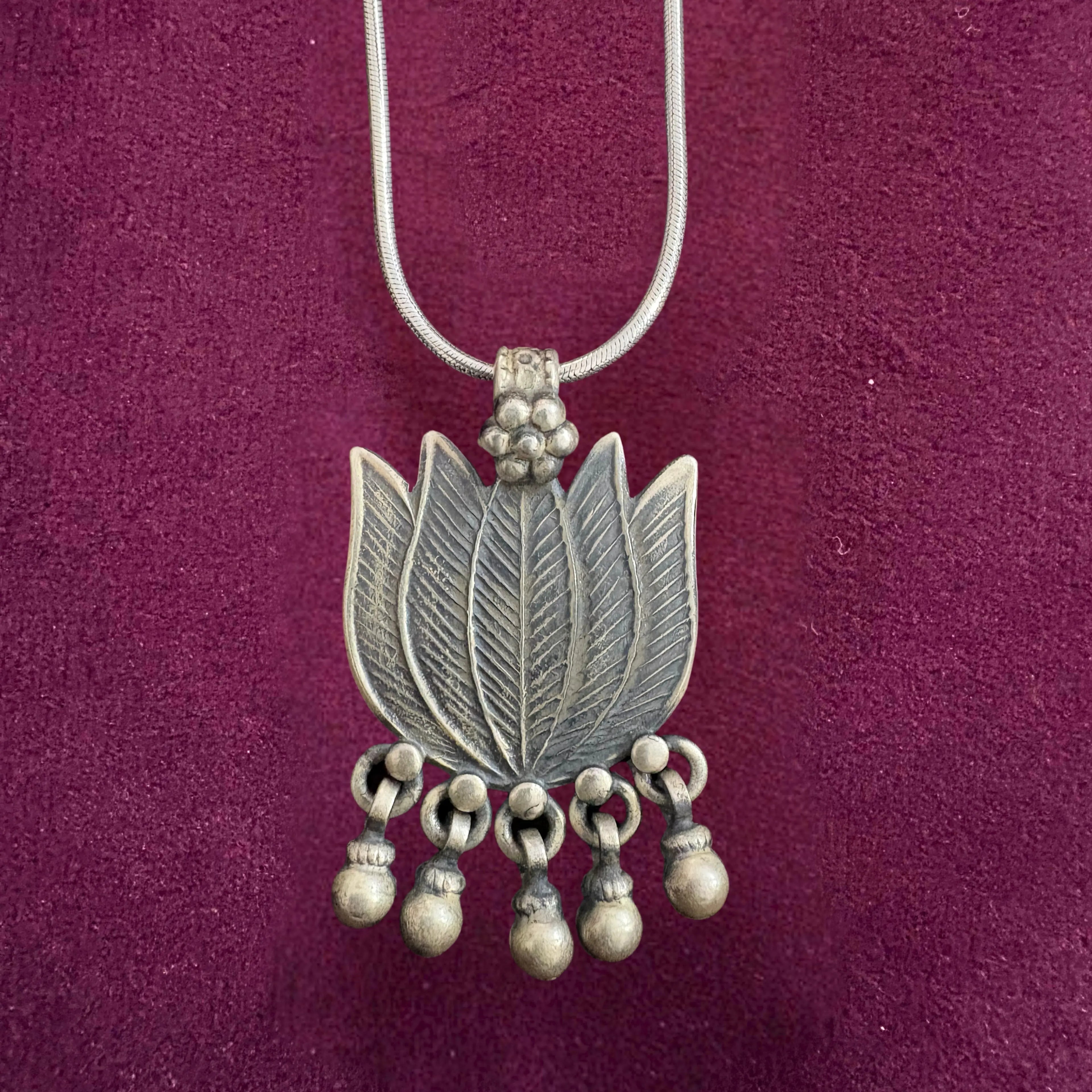 Silver necklace with a lotus-shaped pendant on a maroon background