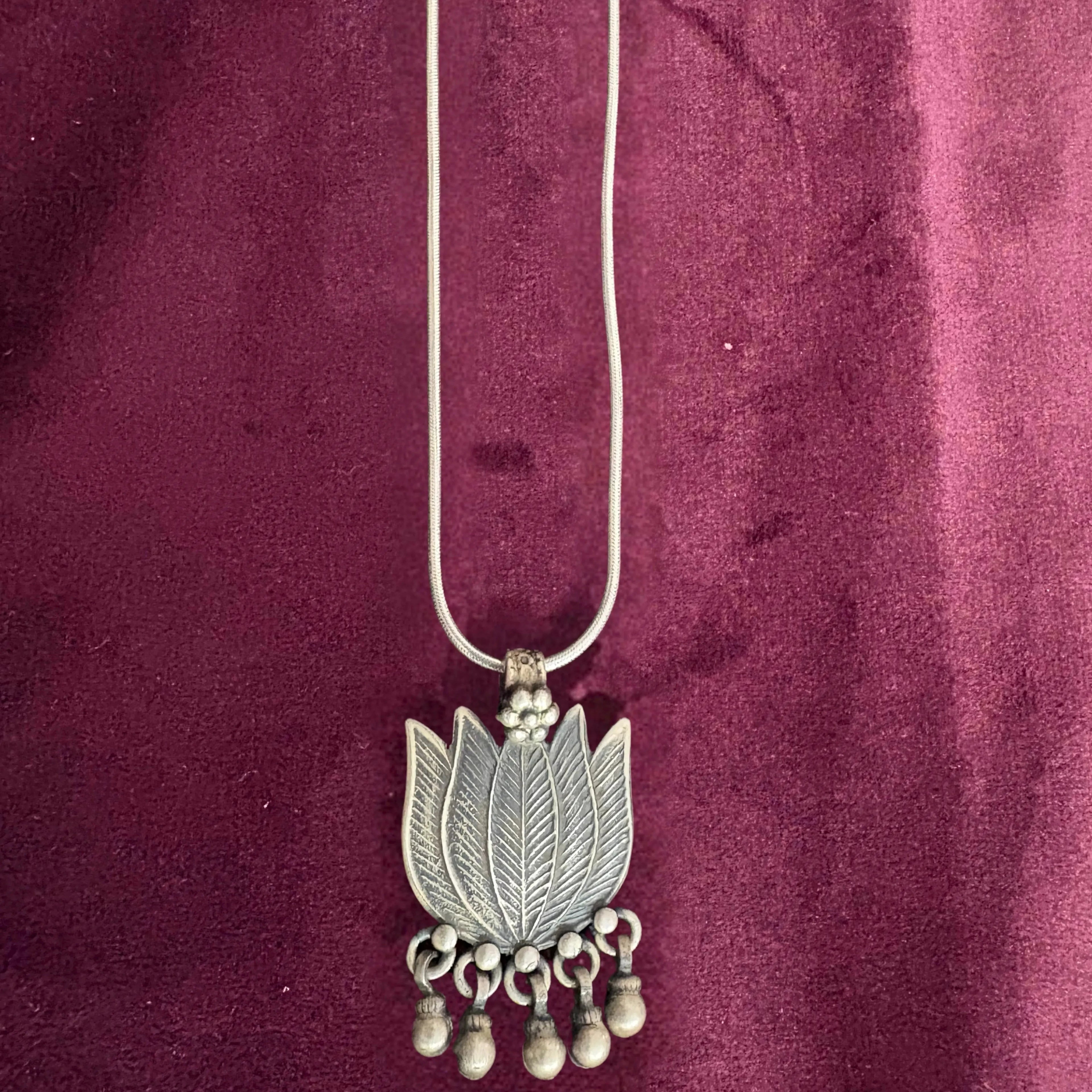 Silver necklace with a lotus-shaped pendant on a maroon fabric background