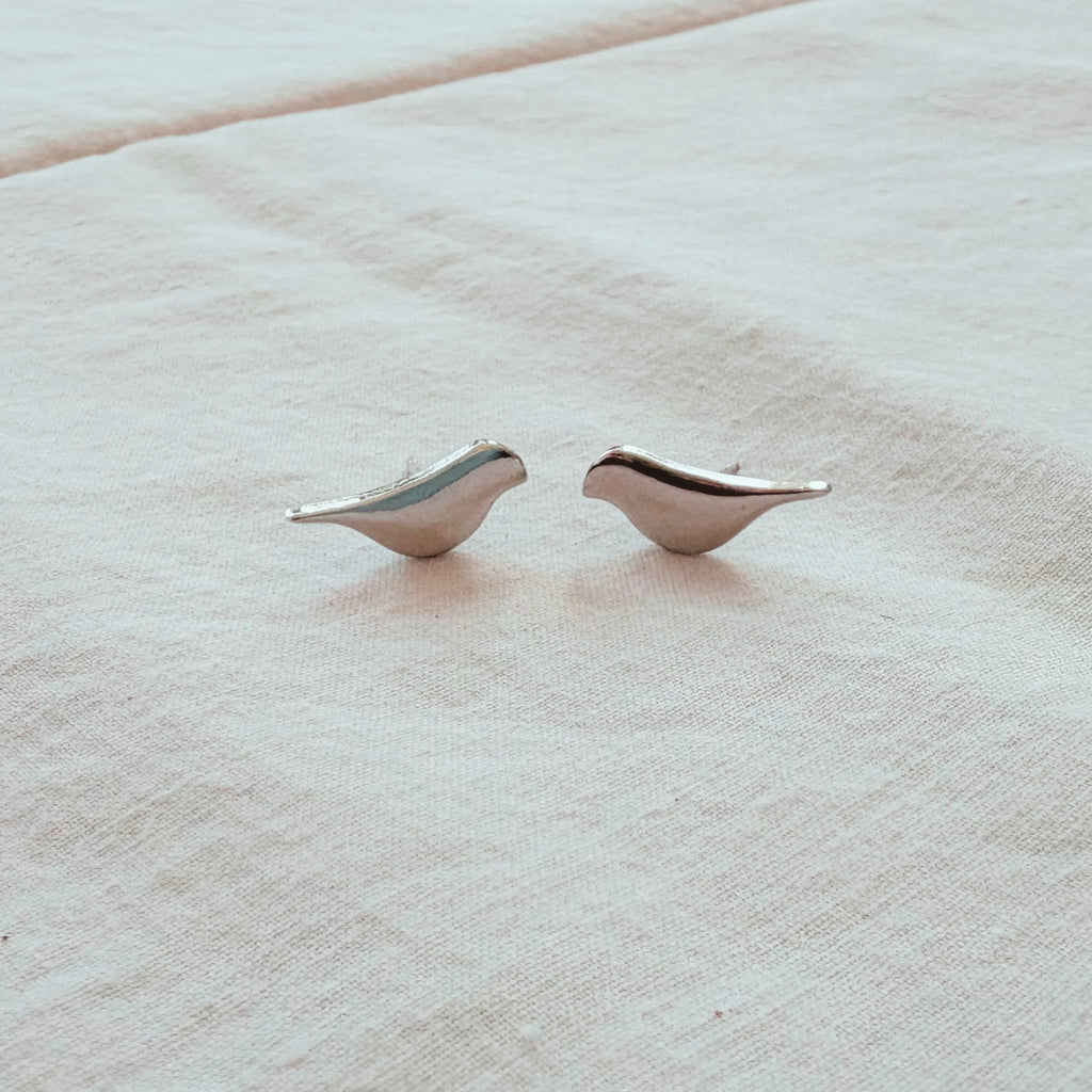 Pair of silver bird-shaped earrings on a beige fabric background