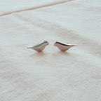 Pair of silver bird-shaped earrings on a beige fabric background