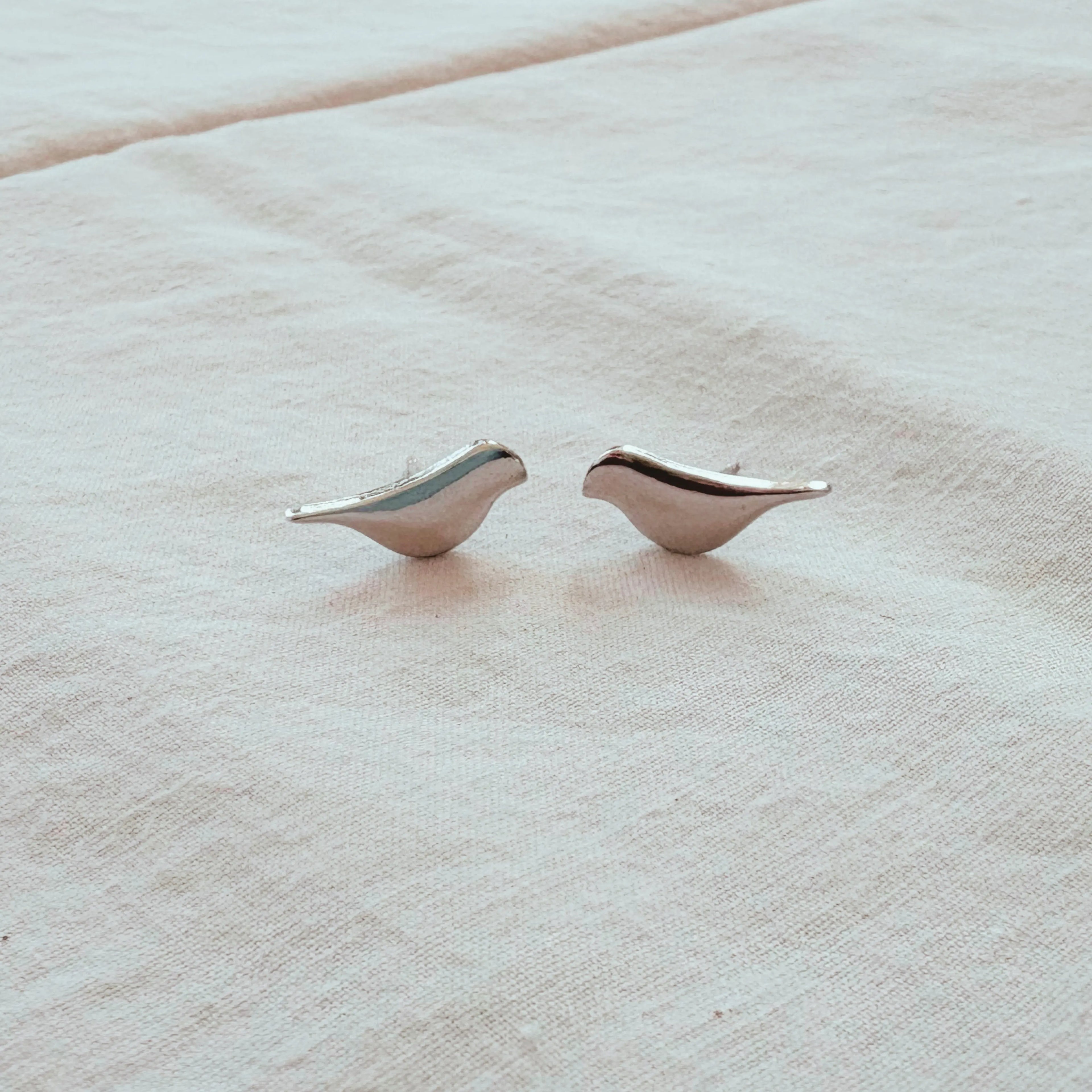 Pair of silver bird-shaped earrings on a beige fabric background