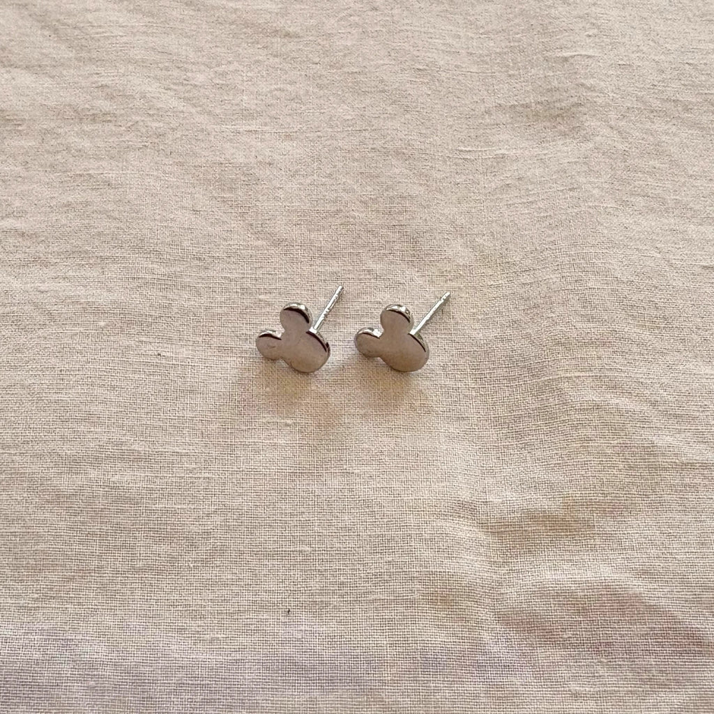 Silver mickey mouse earrings on a beige fabric background