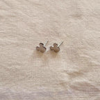 Silver mickey mouse earrings on a beige fabric background