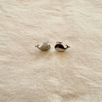 Two small whale-shaped earrings on a beige fabric background
