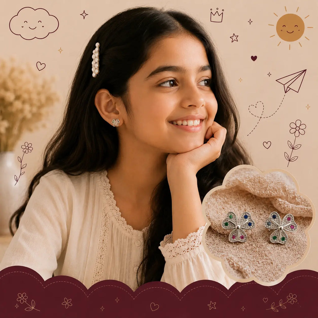 A young girl with long dark hair smiles while wearing a small silver earring with colorful rhinestones. The image includes an inset showing a pair of matching four-leaf clover stud earrings on a soft beige fabric, set against a decorated beige background with doodles of clouds, stars, and a sun.