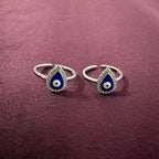 Pair of silver toe rings with blue teardrop designs on a maroon background