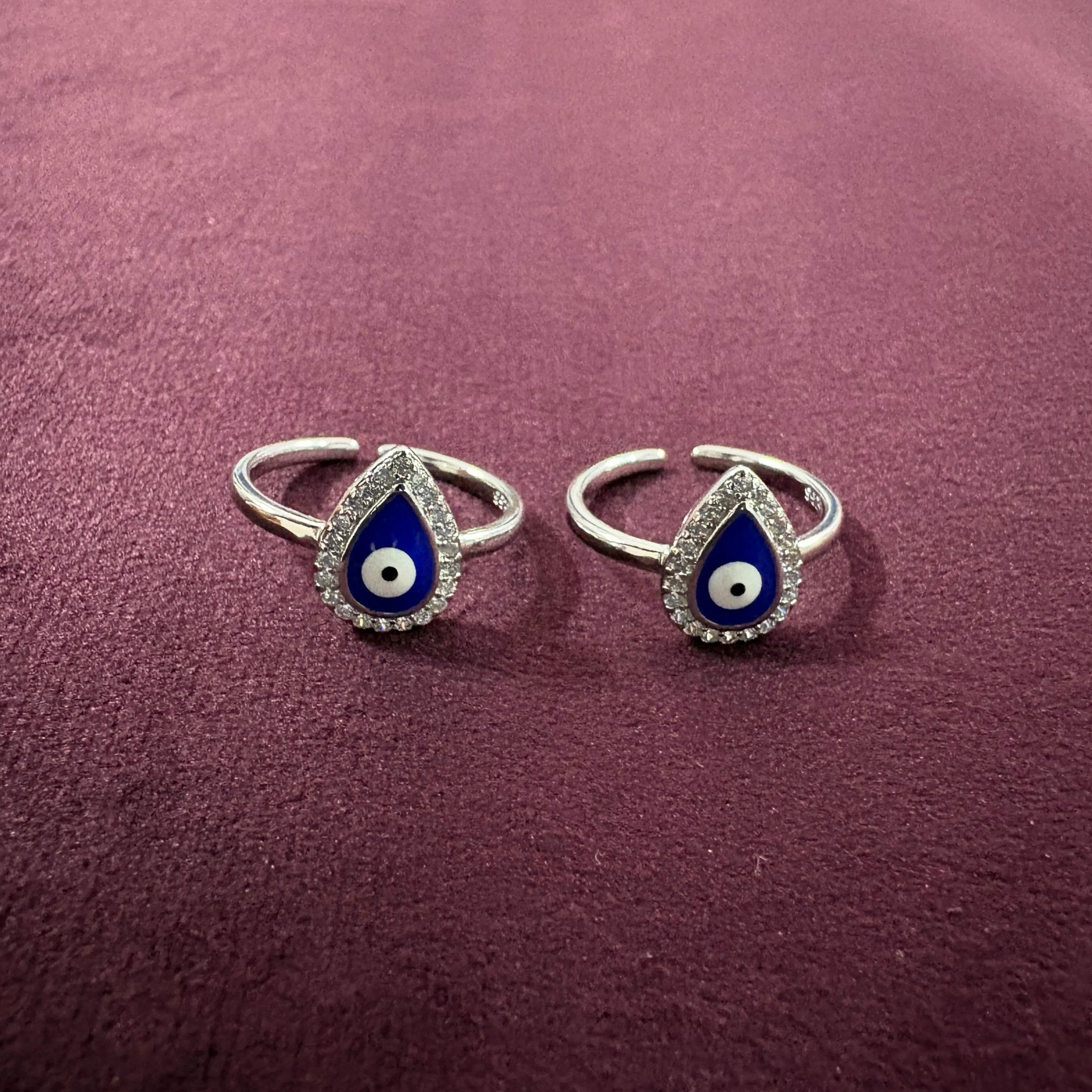 Pair of silver toe rings with blue teardrop designs on a maroon background