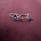 Silver toe rings with blue and white evil eye design on a maroon  background