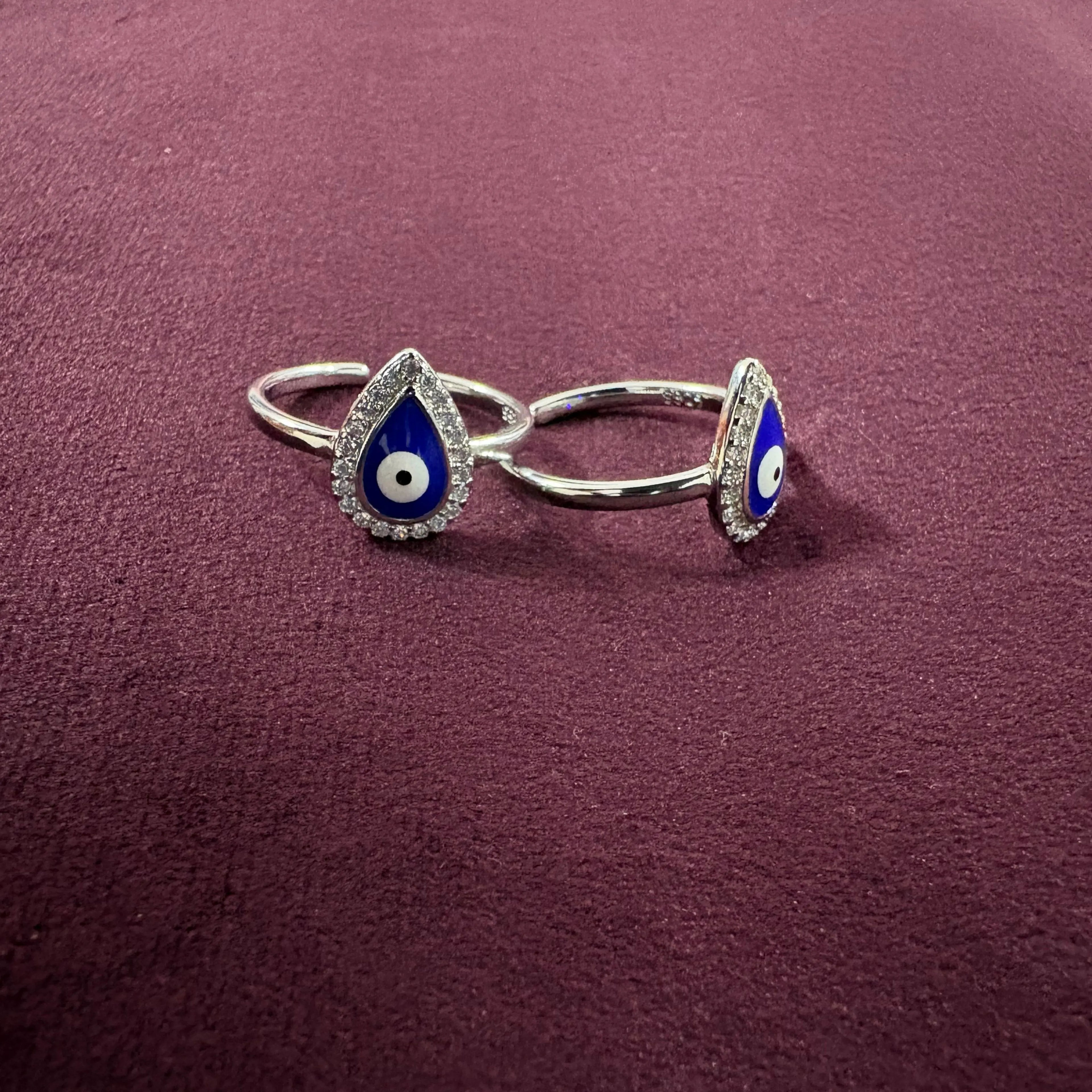 Silver toe rings with blue and white evil eye design on a maroon  background