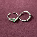 Flat lay image of Dual Arch Emerald Toe Rings on maroon background