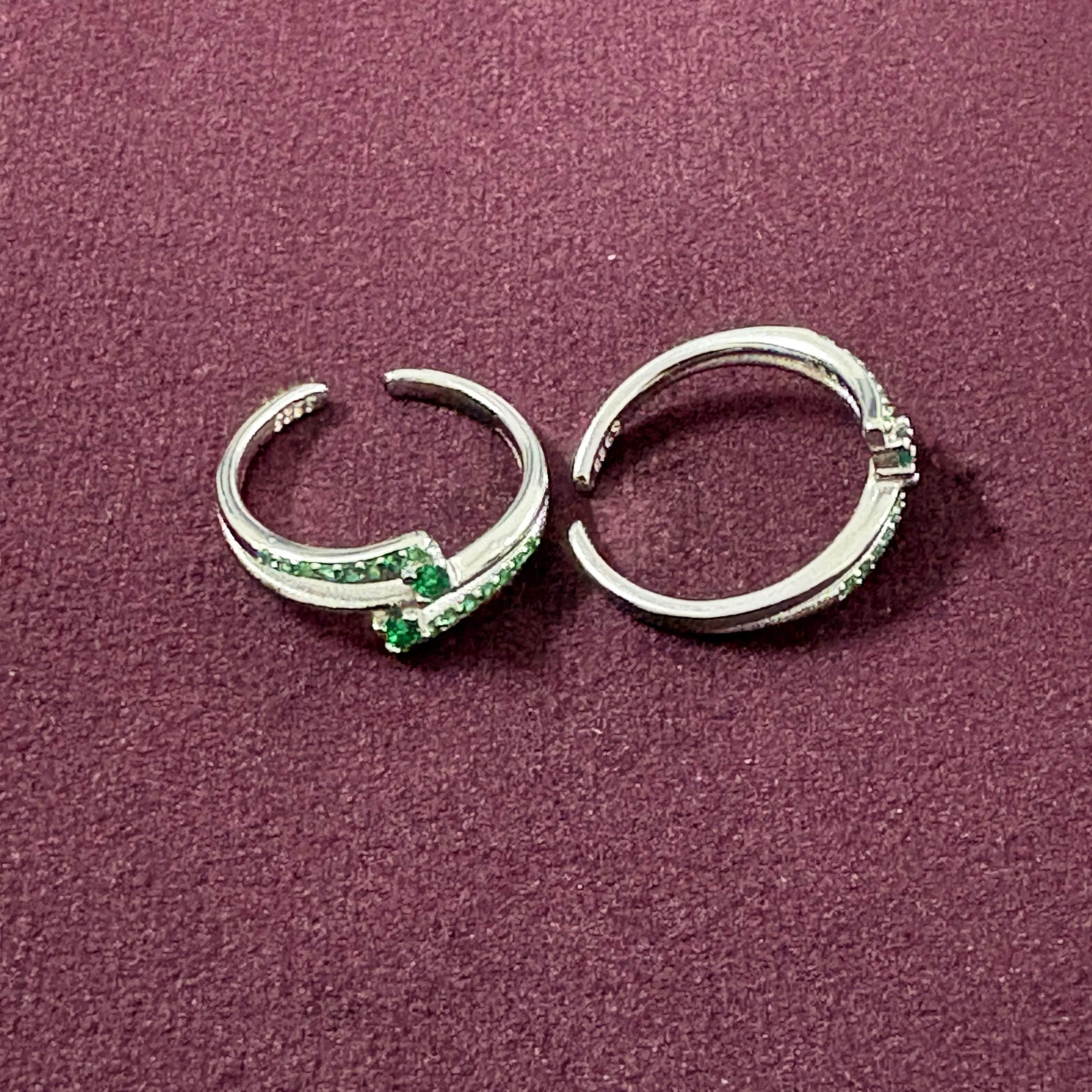 Flat lay image of Dual Arch Emerald Toe Rings on maroon background