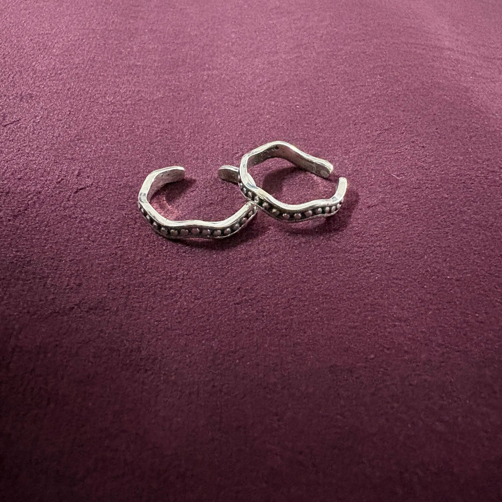 Flat lay image of Wavy Beaded Oxidized Band Toe Rings on maroon background