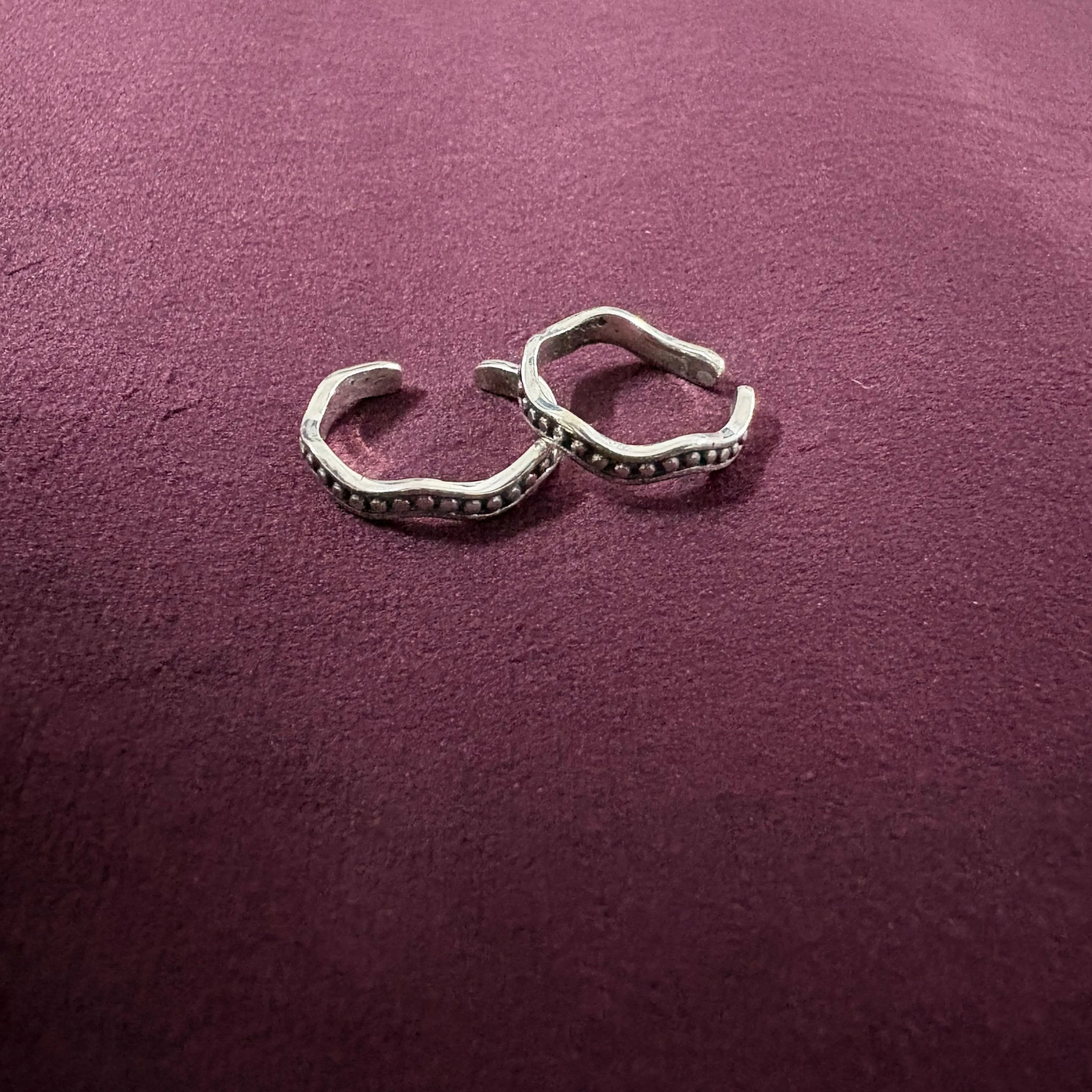 Flat lay image of Wavy Beaded Oxidized Band Toe Rings on maroon background