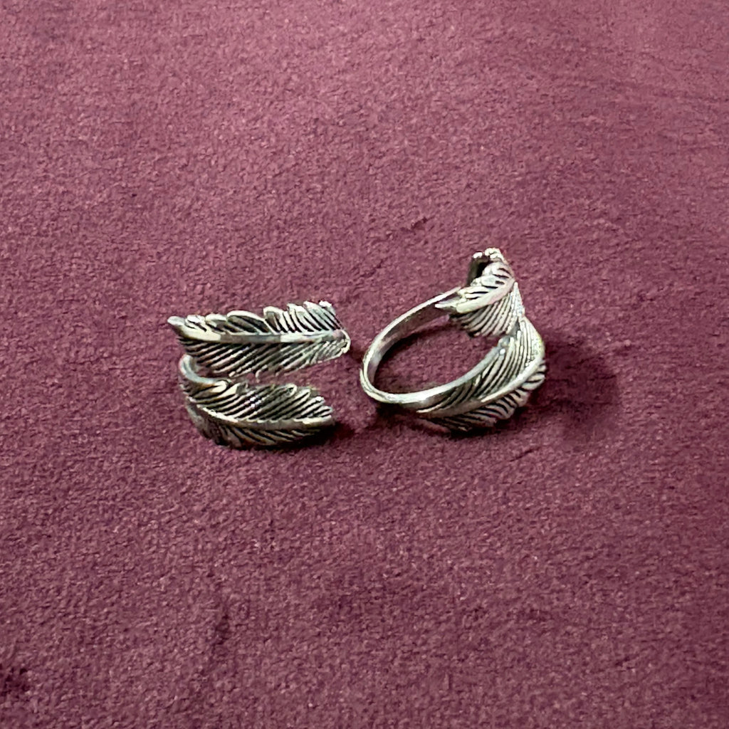 Flat lay image of Double Feather Oxidized Bypass Toe Rings on maroon background