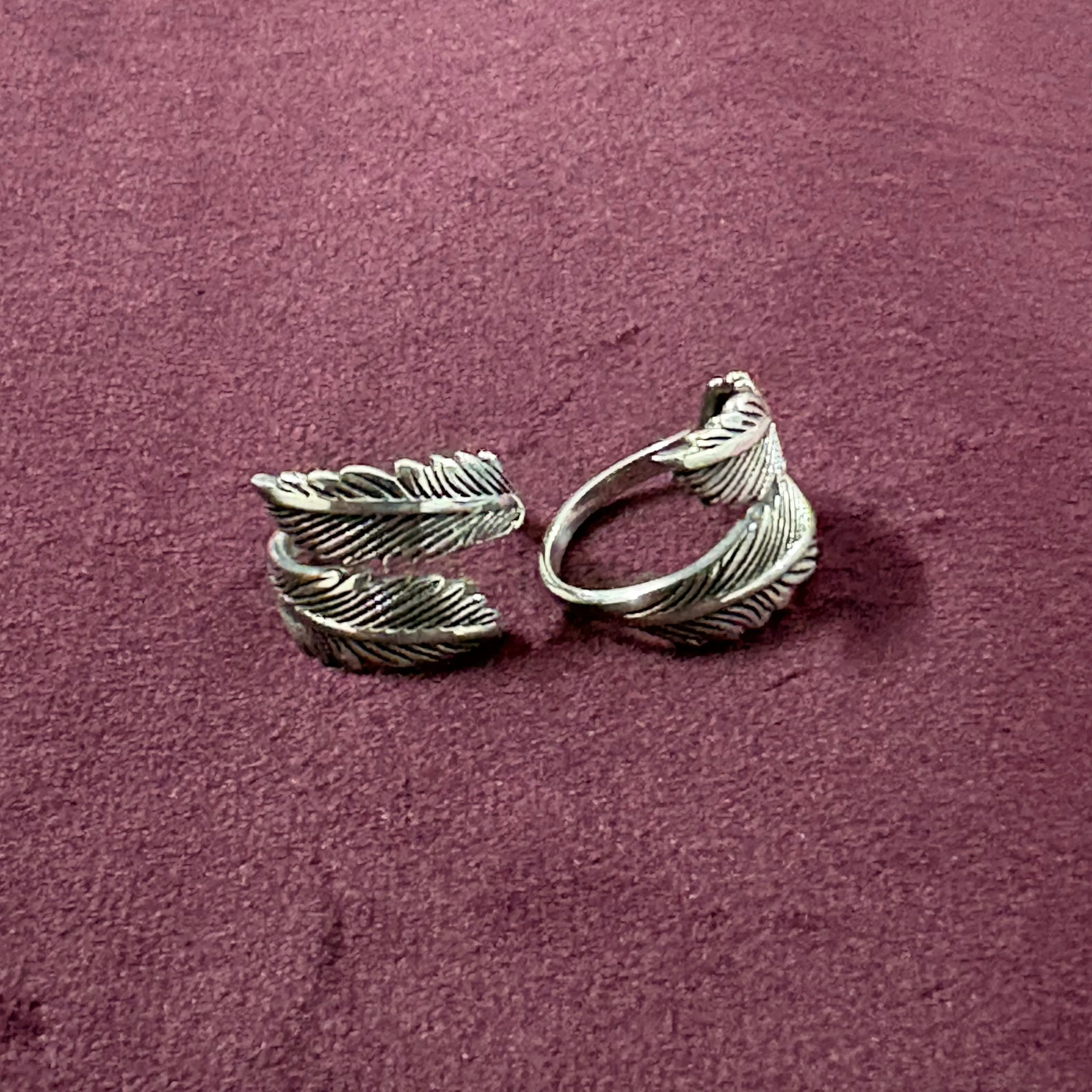 Flat lay image of Double Feather Oxidized Bypass Toe Rings on maroon background