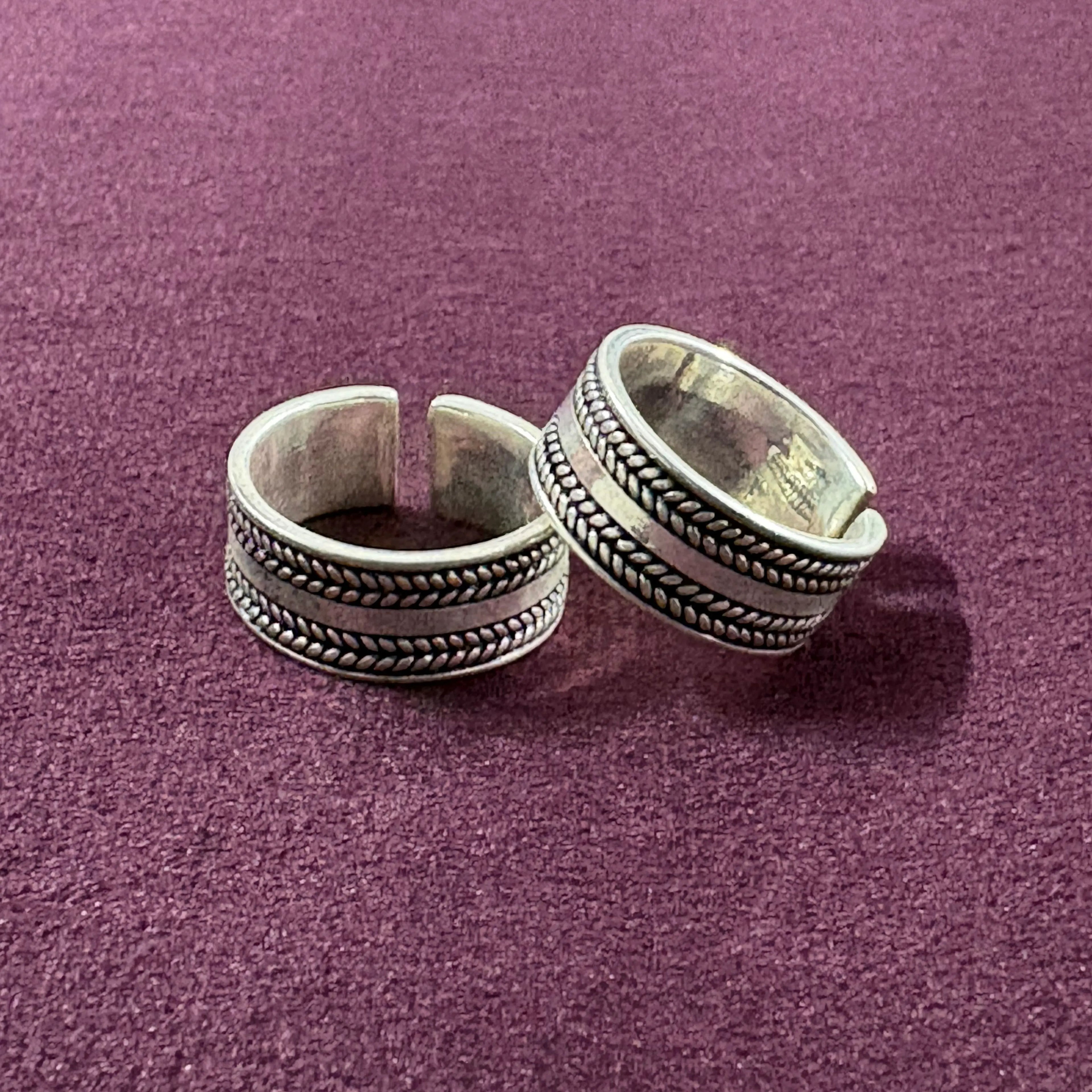 Flat lay image of Braided Oxidized Band Toe Rings on maroon background