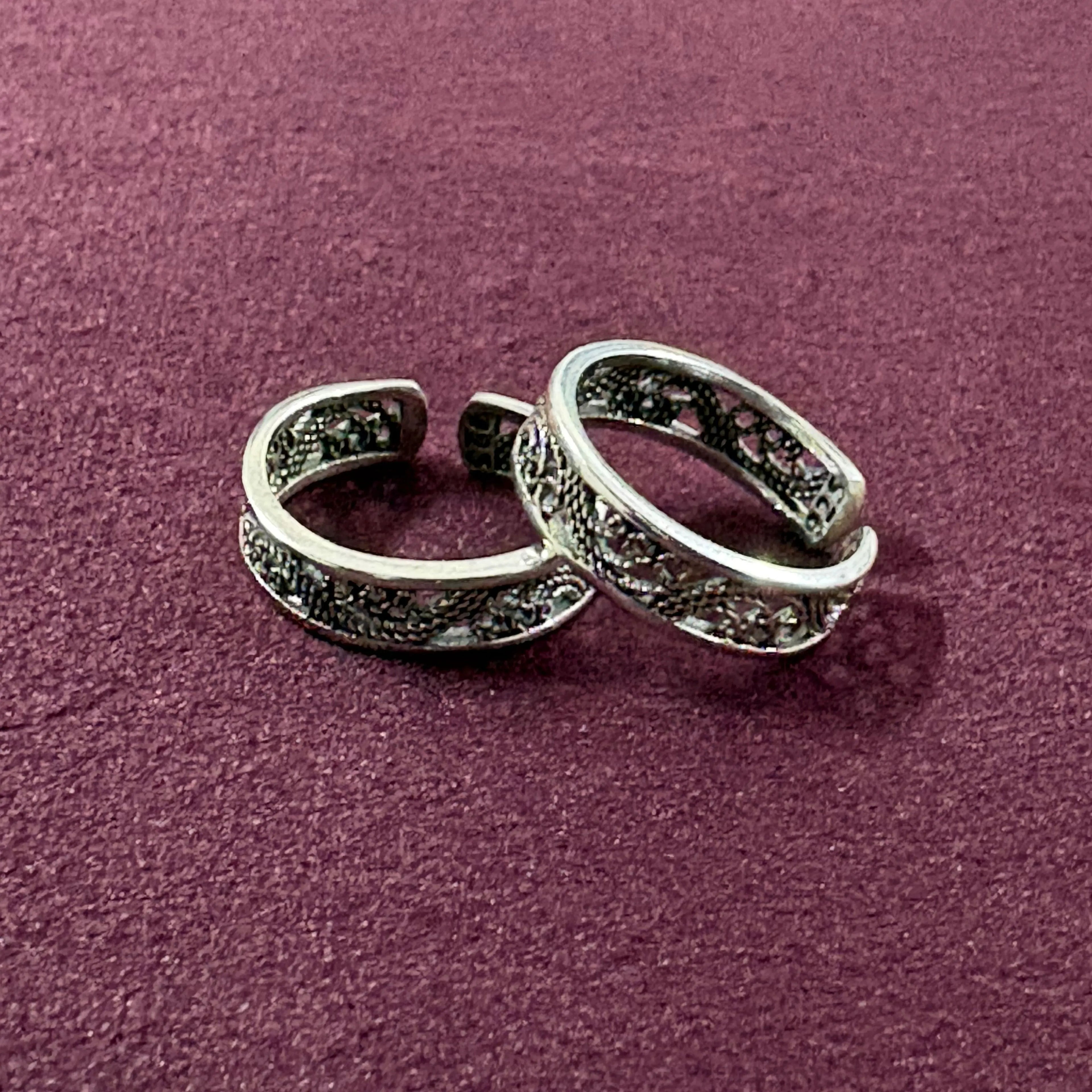 Flat lay image of Intricate Filigree Oxidized Toe Rings on maroon background