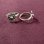 Flat lay image of Wire Flower petal toe ring on maroon background