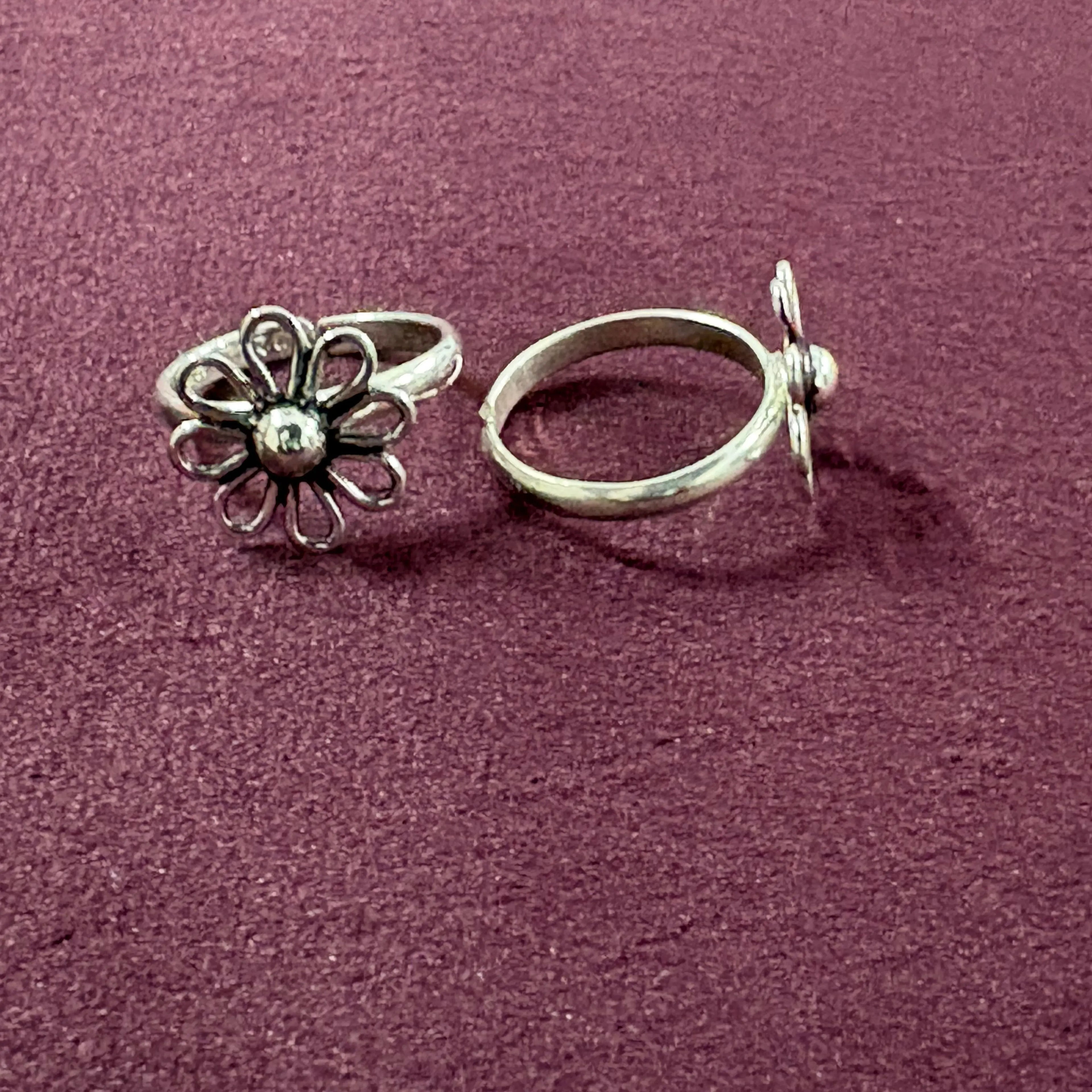 Flat lay image of Wire Flower petal toe ring on maroon background