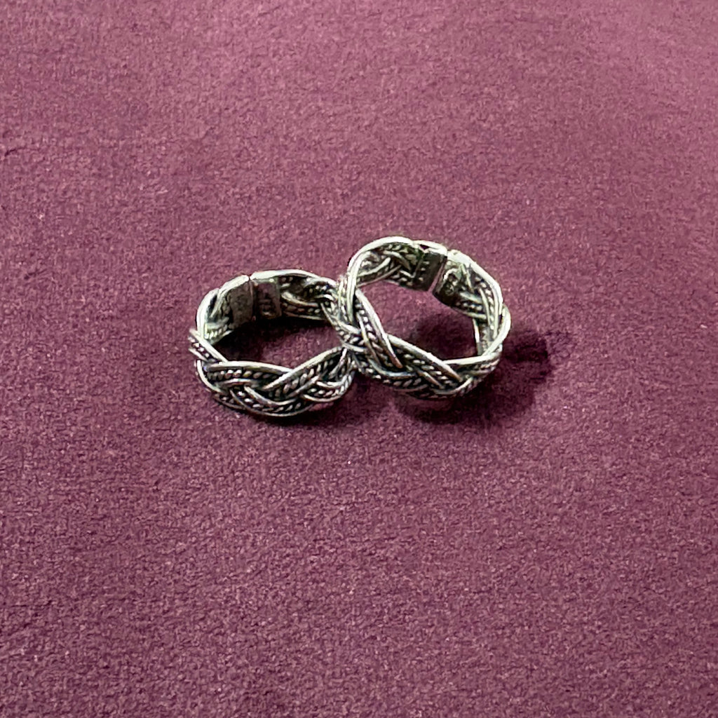 Flat lay image of Braided Filigree Oxidized Band Toe Rings on maroon background